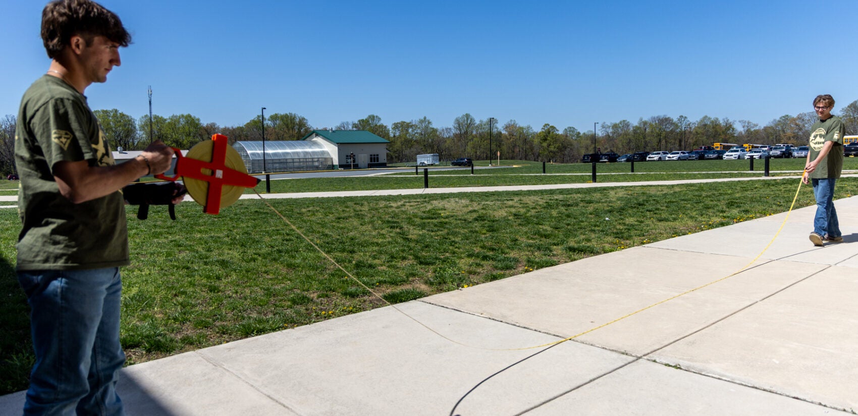 Two students stand far apart from each other holding a measuring tape between them