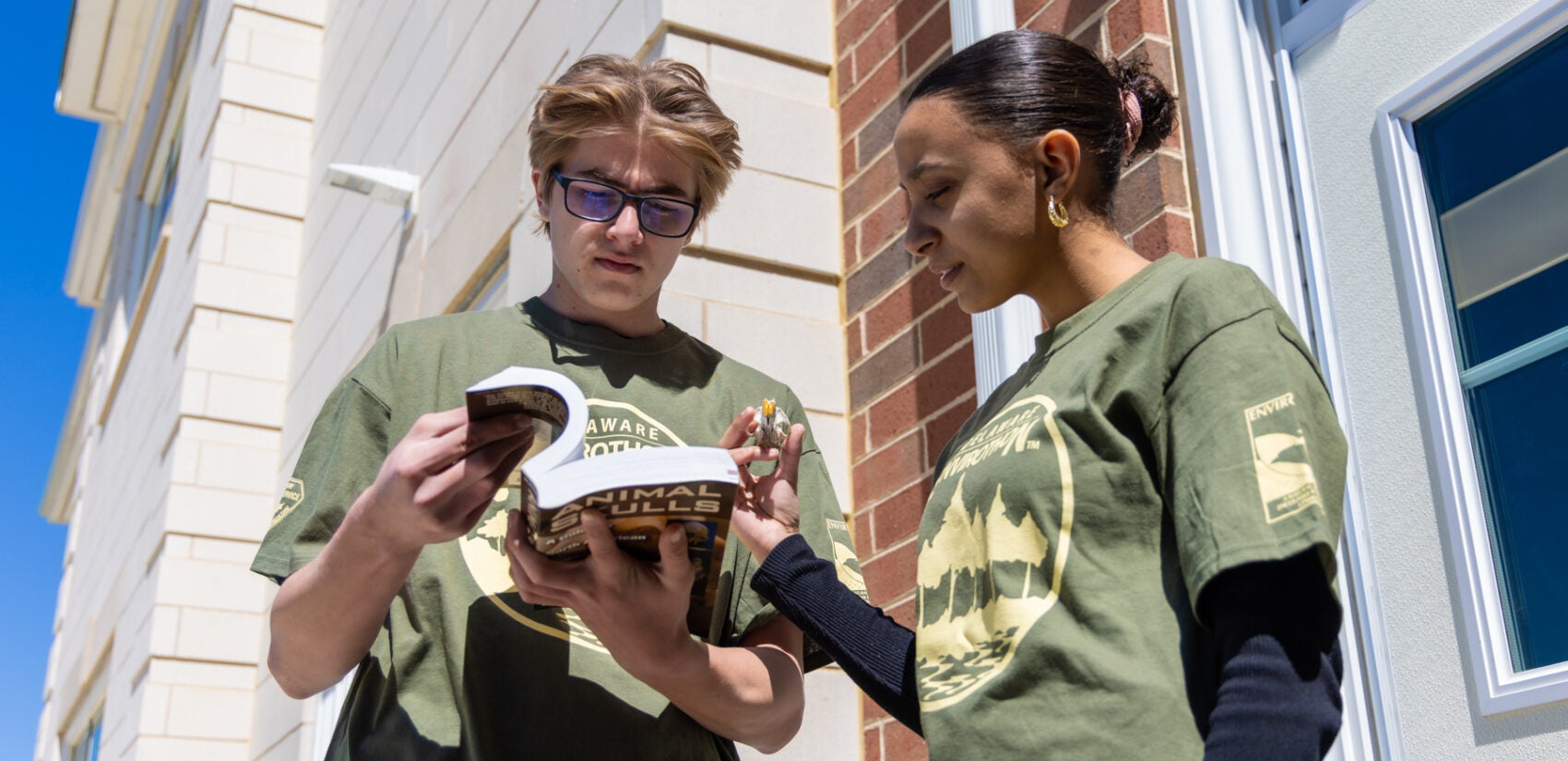 Two students standing outdoors looking at a book together