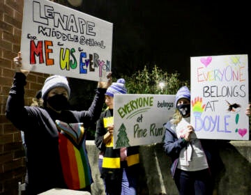 Demonstrators hold sign sin support of LGBTQ people outside a school board meeting
