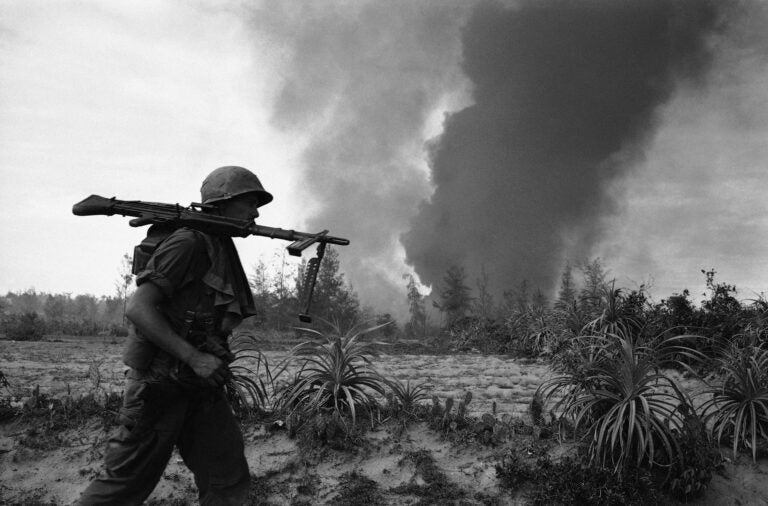 A U.S. Infantryman of the 25th division balances a M60 machine gun on his shoulder as he rushes into position behind smoke rising from a burning village near Duc Pho, about 325 miles North of Saigon on July 31, 1967. Air strikes had been called in on the village when elements of the division met resistance during a search and clear operation. (AP Photo)