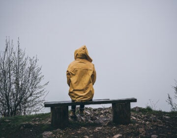 Sad depressed woman sitting on bench in raincoat