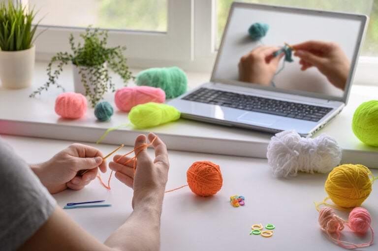 A man is crocheting and watching a tutorial video. (Ramil Gibadullin/Bigstock)