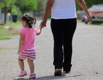 A young girl walking down the street holding onto a woman's hand
