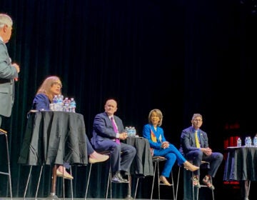 A moderator on stage with 5 panelists for the town hall