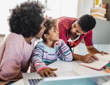 Two parents help their child for their homework.