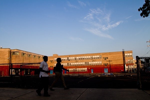 Students walk on their way to school in the early morning. The school building is visible in the background.