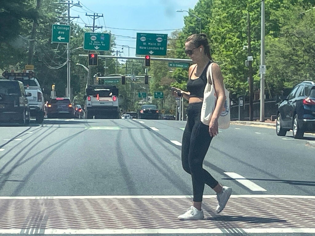 A University of Delaware student looks at a phone while crossing Main Street