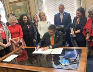 Matt Meyer signing a paper on his desk, surrounded by people