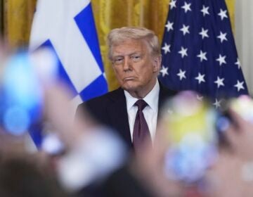 Donald Trump sitting in front of American and Greek flags