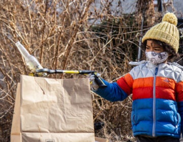 Eiji Mizukane places a glass bottle into a paper trash bag during a North Philly cleanup